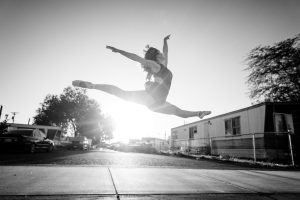 black and white image ballet dancer leaping with sun behind